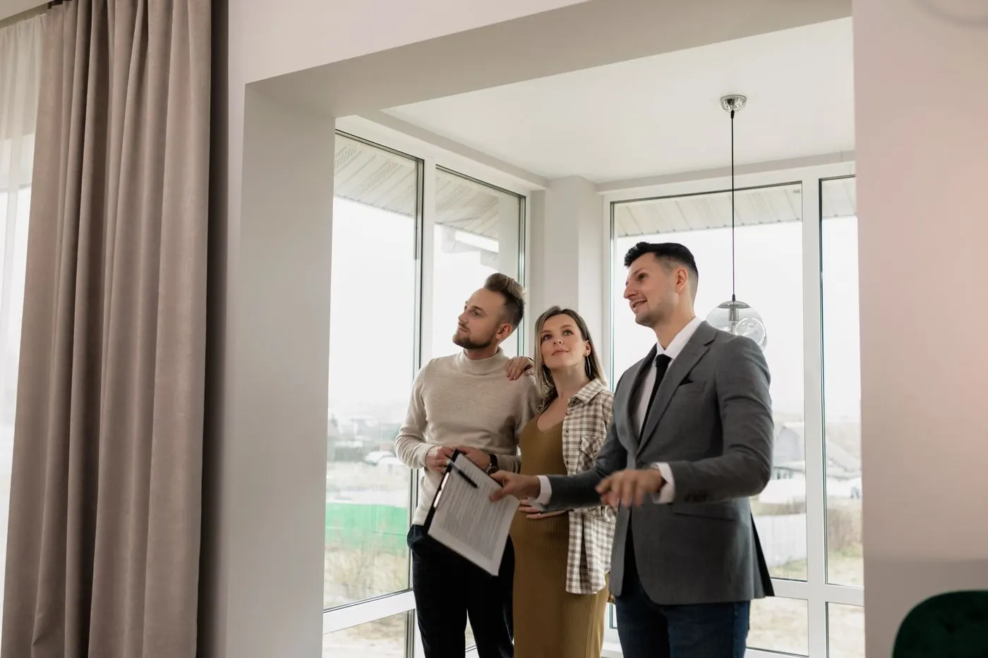Un agent immobilier présente un bien à un couple, devant une baie vitrée